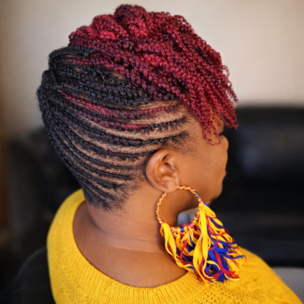 Lady with braided hair wearing a yellow sweater and colorful earrings.