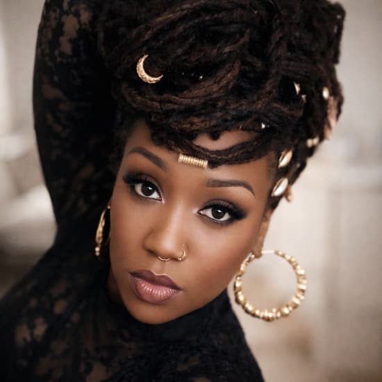 Photo of a woman with styled locs hair, weariing fashionable jewelry.